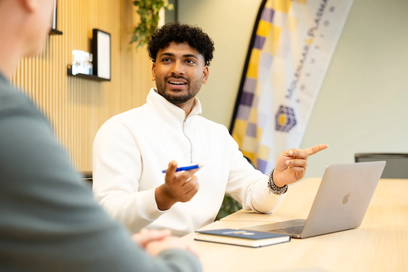 Gianluca aan tafel, wijzend naar zijn laptop, in gesprek